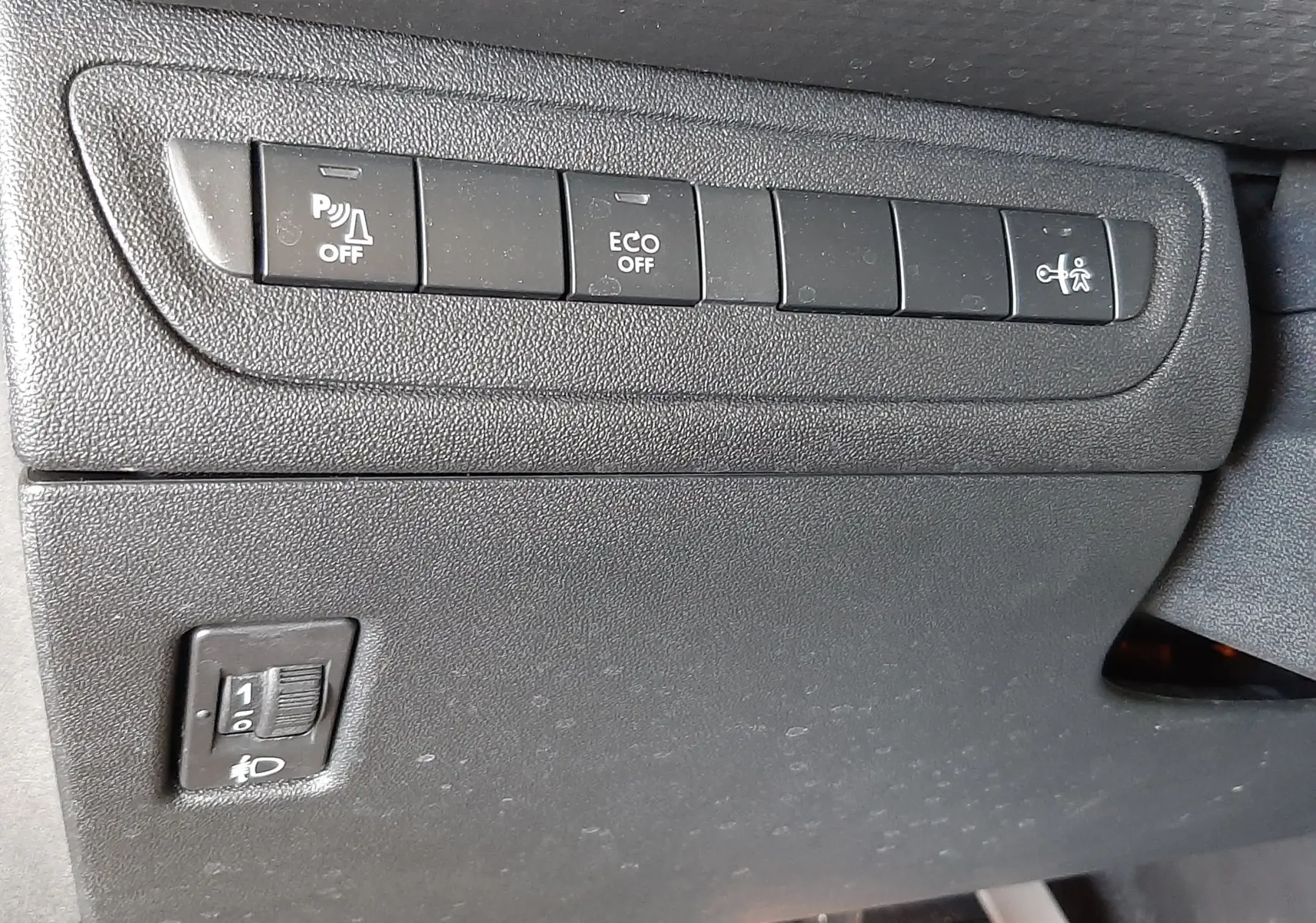 Gros plan sur les commandes de fonctions et réglage des phares sous le tableau de bord d'une Peugeot 2008 GT Line 2019.