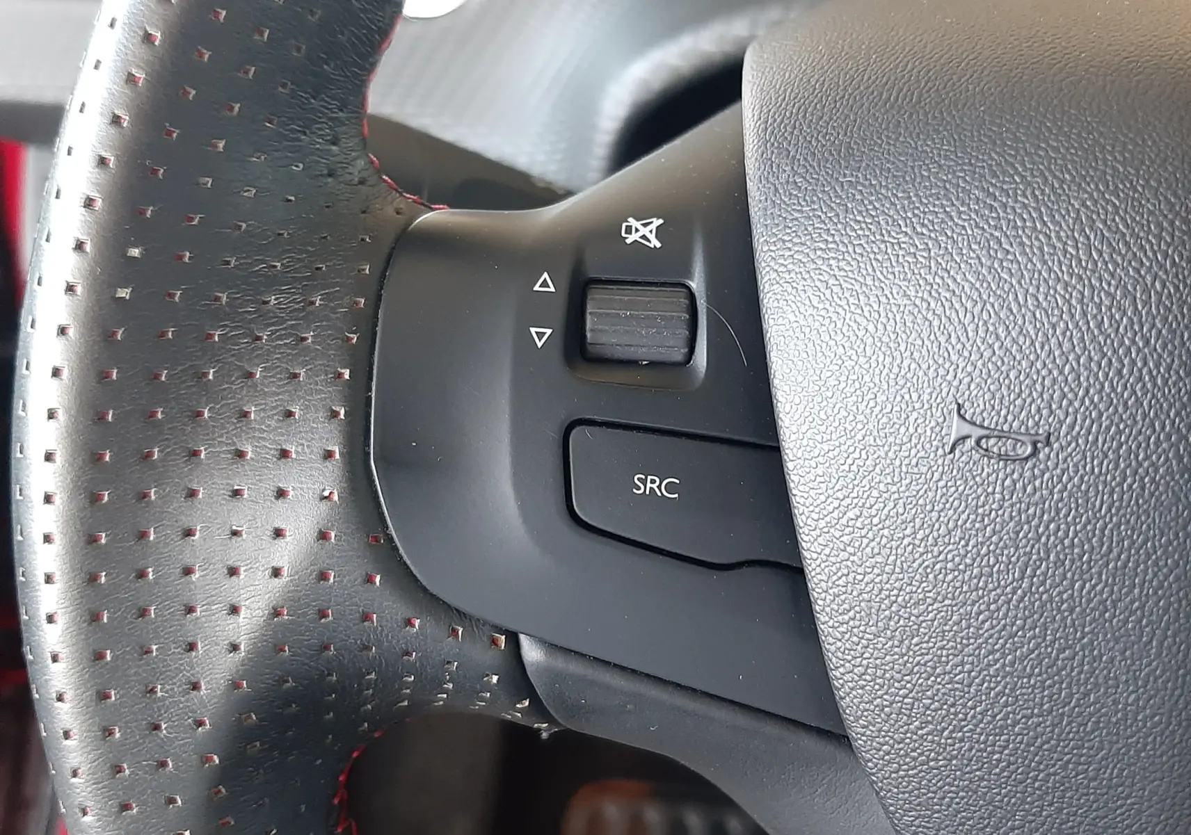 Gros plan sur la commande sonore du volant en cuir perforé avec surpiqûres rouges d'une Peugeot 2008 rouge Ultimate Metal 2019.