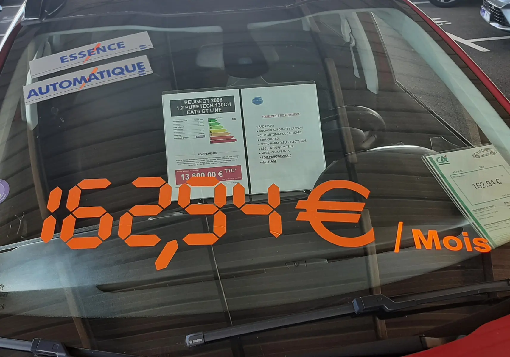 Vue avant d'une Peugeot 2008 rouge Ultimate Metal avec affichage du prix mensuel sur le pare-brise.