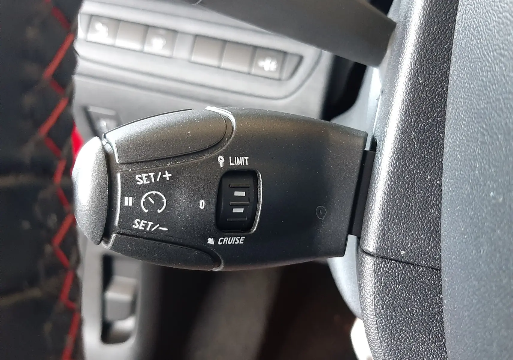 Gros plan sur la commande de régulateur de vitesse noire dans l'habitacle d'une Peugeot 2008 rouge Ultimate Metal.