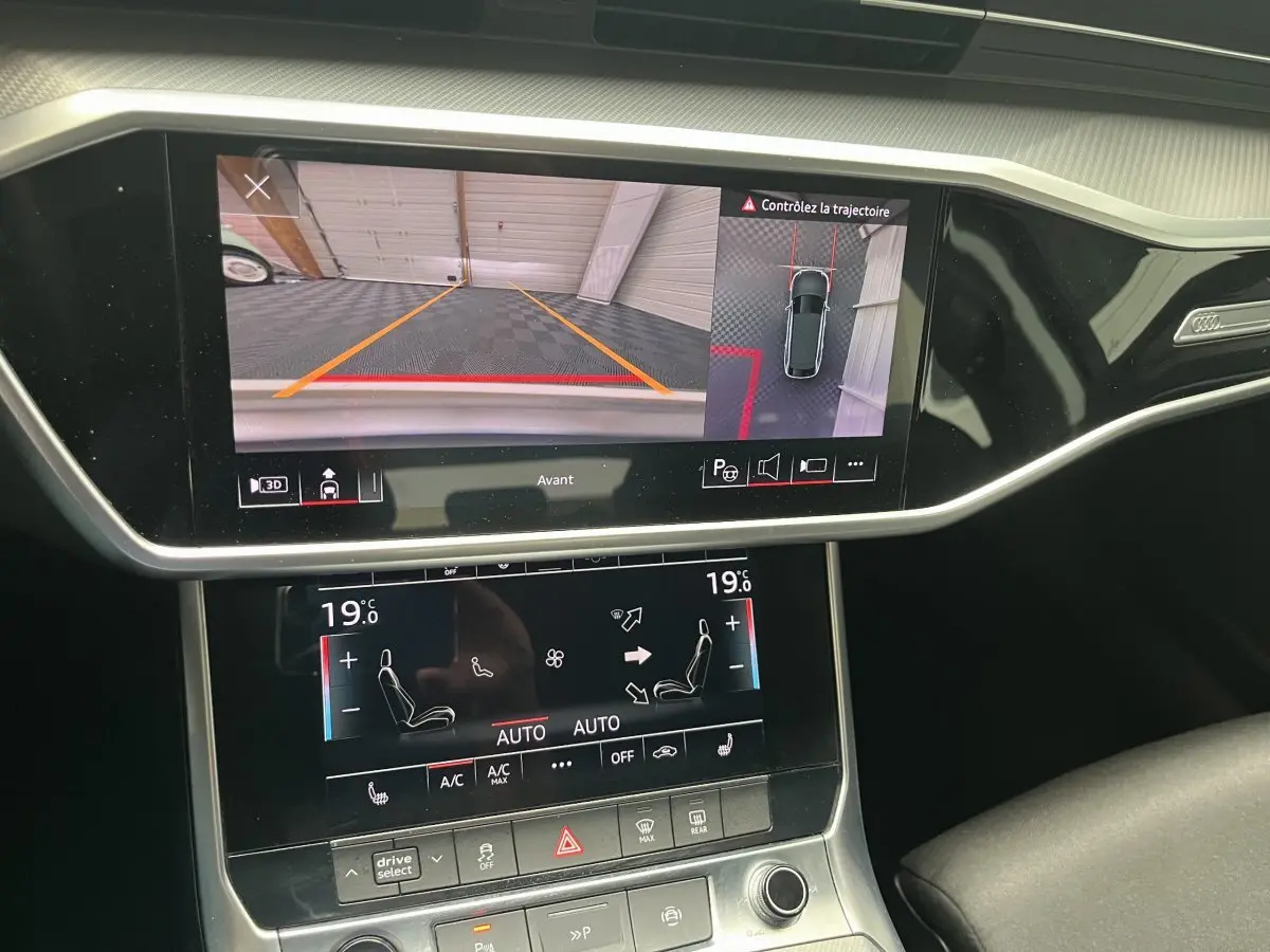 Vue rapprochée de l'écran tactile du tableau de bord d'une Audi A6 noire, affichant la caméra avant et la climatisation digitale.