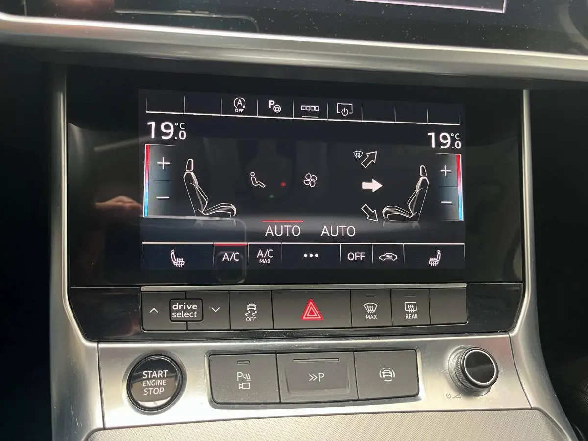 Tableau de bord tactile de l'Audi A6 noir, affichant la climatisation bi-zone à 19°C en vue frontale rapprochée.