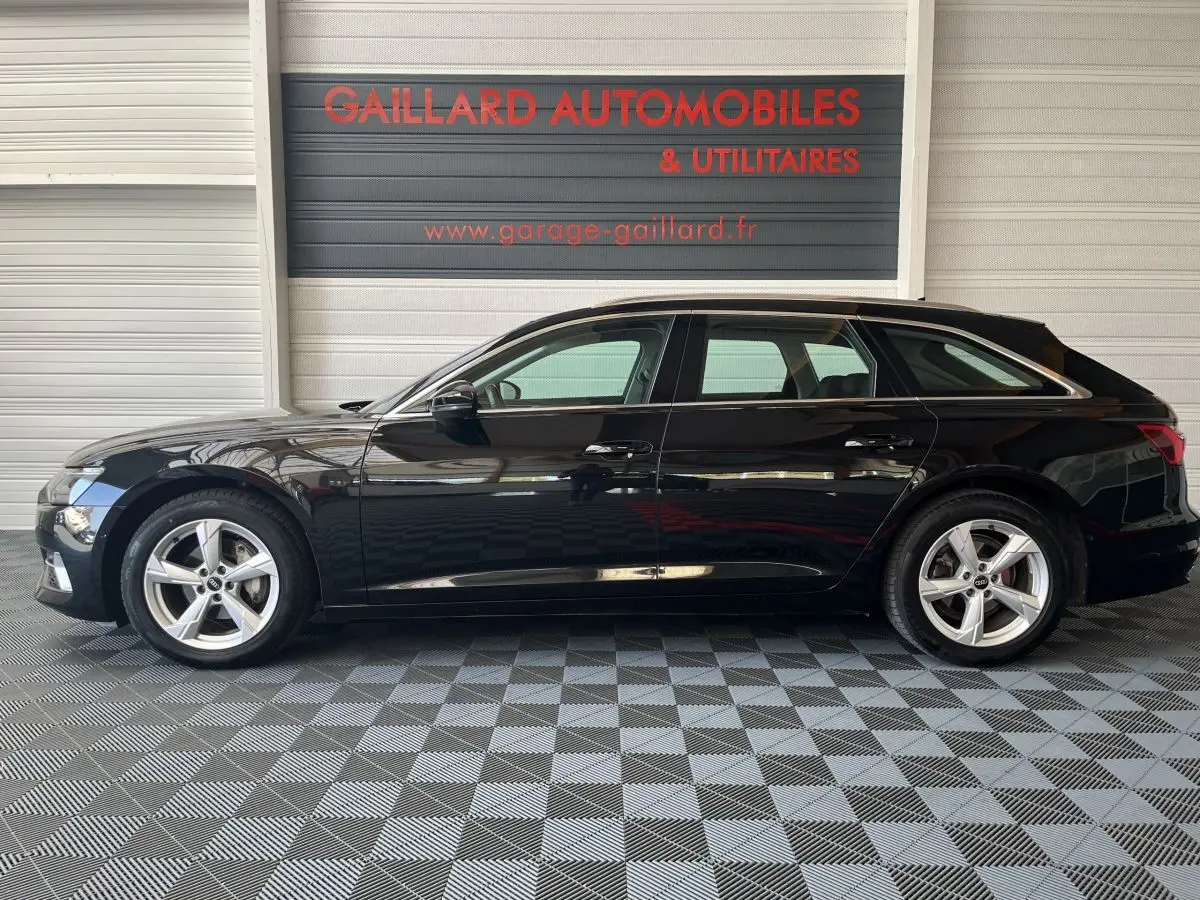 Profil côté gauche d'une Audi A6 noire 2022 garée en intérieur avec jantes alliage et vitres teintées.