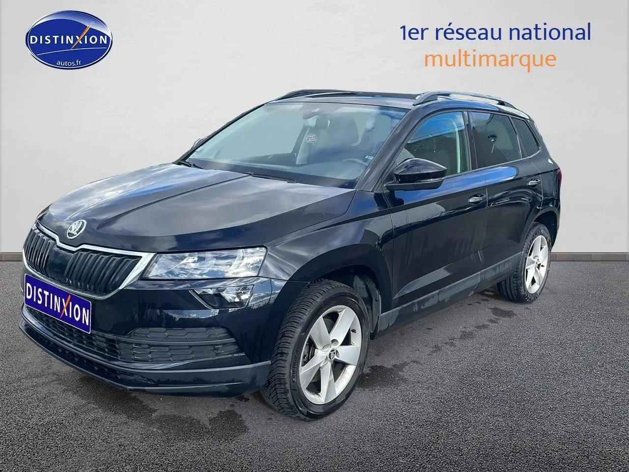 SKODA KAROQ noir vue 3/4 avant droit avec jantes alu et barres de toit sur fond clair.