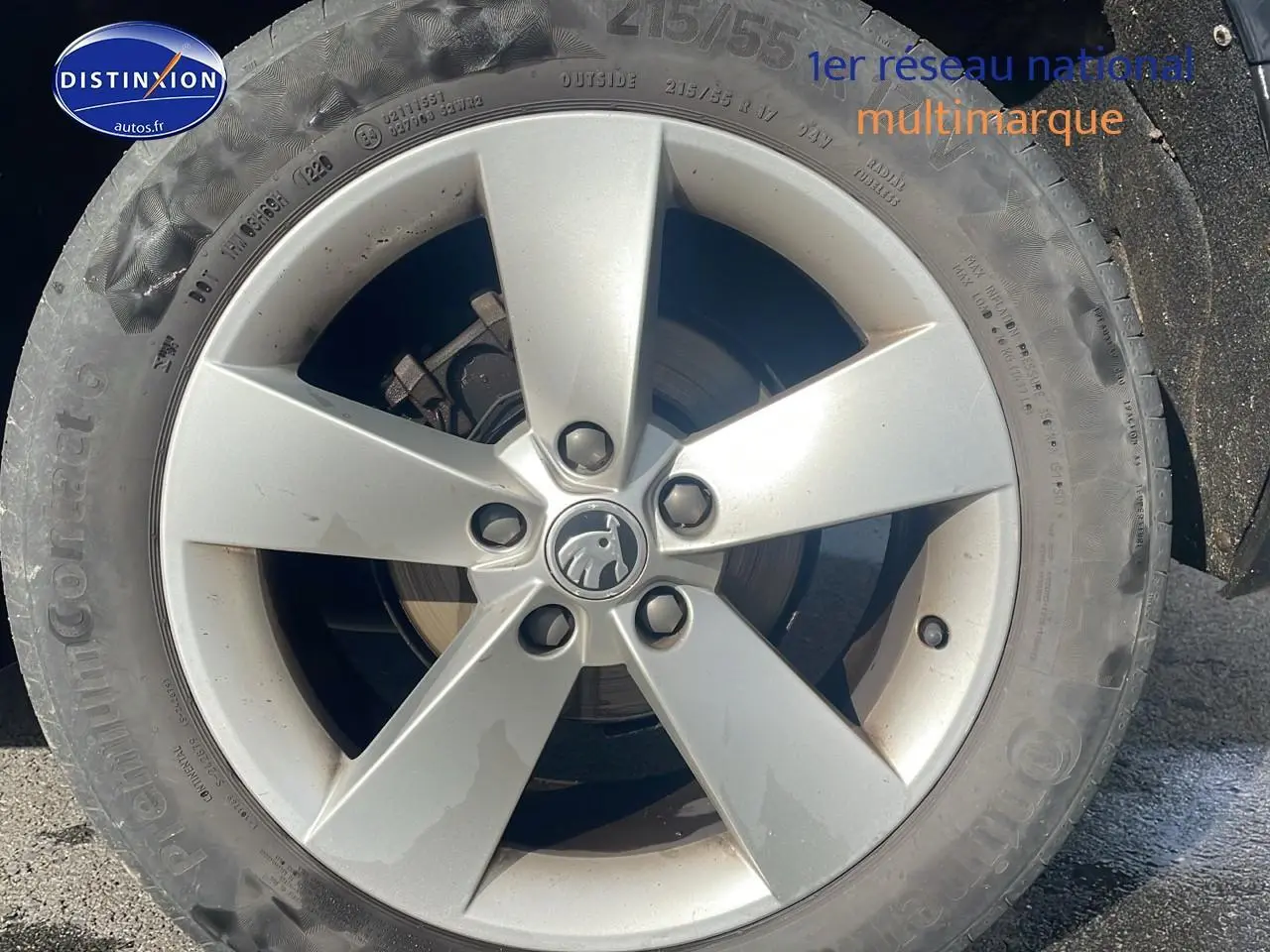 Gros plan sur la jante alu argentée d'une Skoda Karoq noire, mettant en valeur le logo central au soleil.