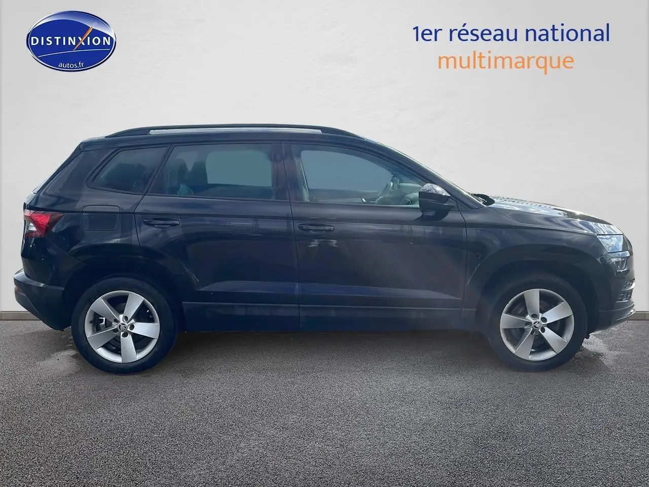 Profil côté gauche d'un SUV SKODA KAROQ noir 2018 avec jantes alu et barres de toit visibles sur fond clair.