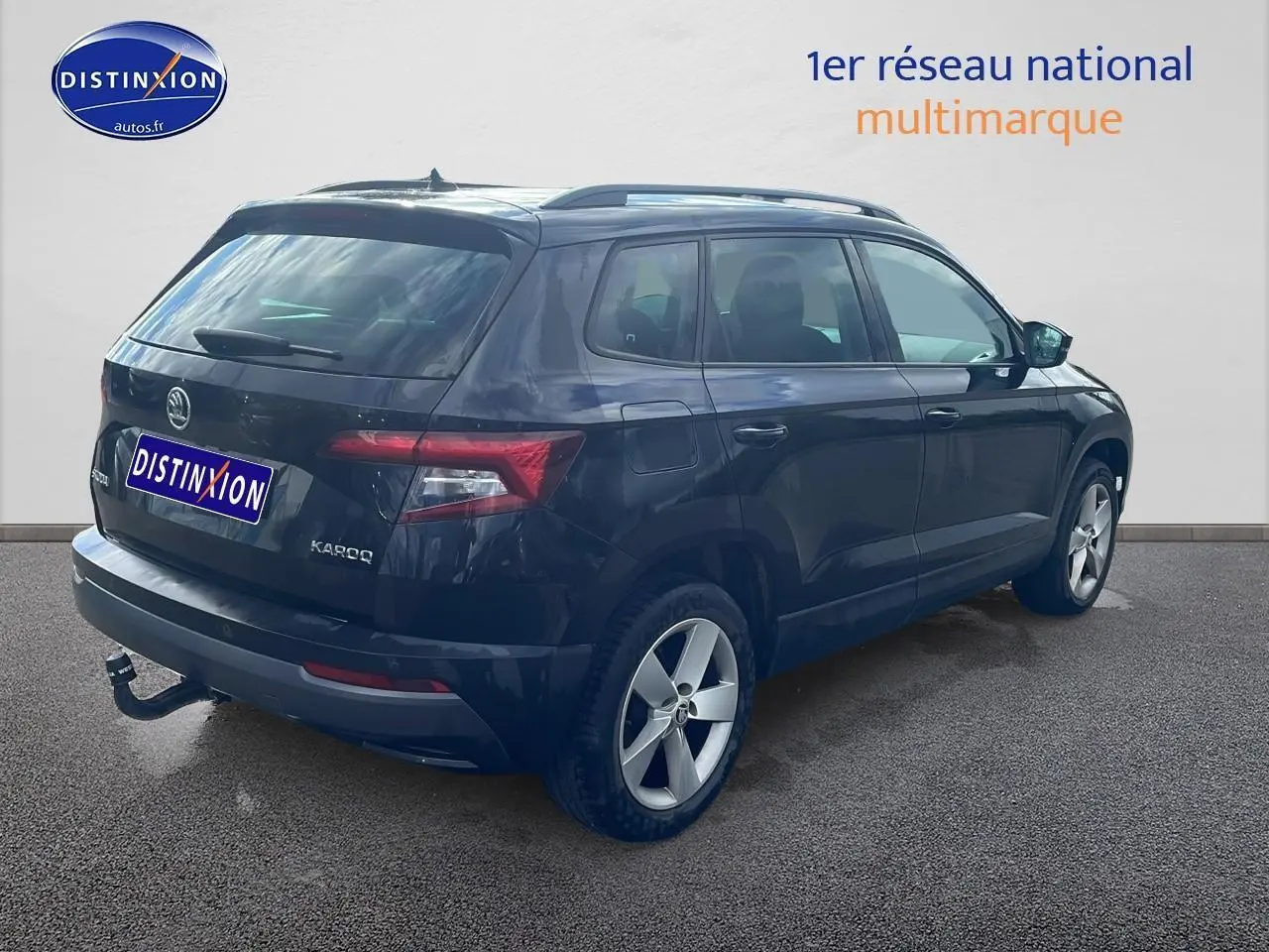 Vue 3/4 arrière droite d'un Skoda Karoq noir avec barres de toit et attelage visible sur un fond neutre.