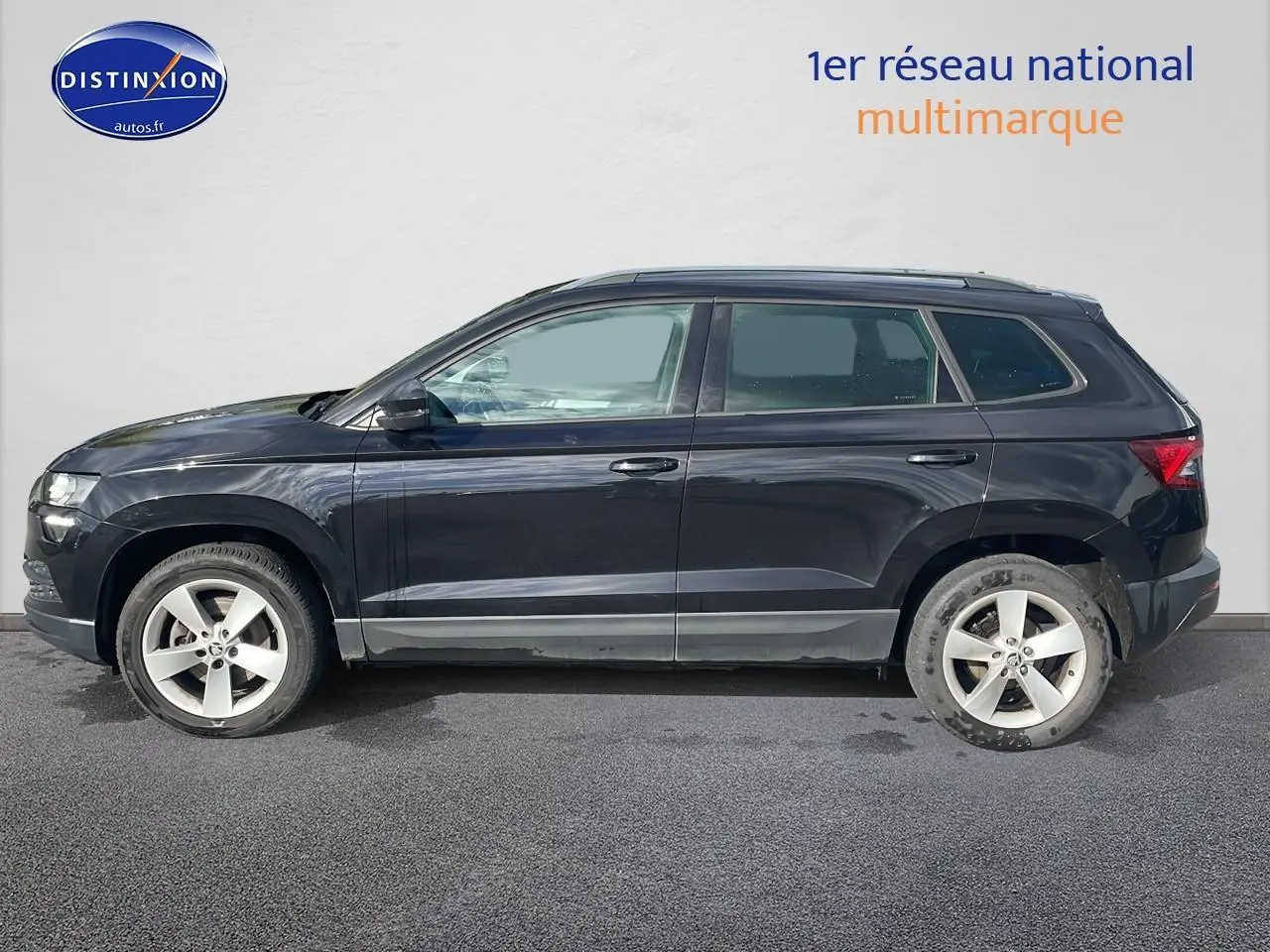 Profil côté gauche d'un Skoda Karoq noir 2018 avec jantes alu et barres de toit visibles sur fond clair.