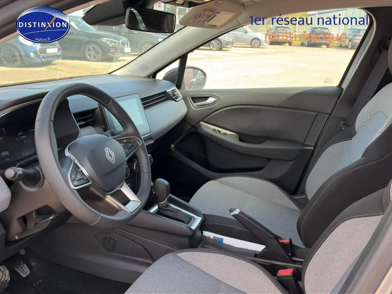 Intérieur de Renault Clio V gris foncé, vue côté conducteur, volant multifonction et sièges tissu gris à motifs 3D.