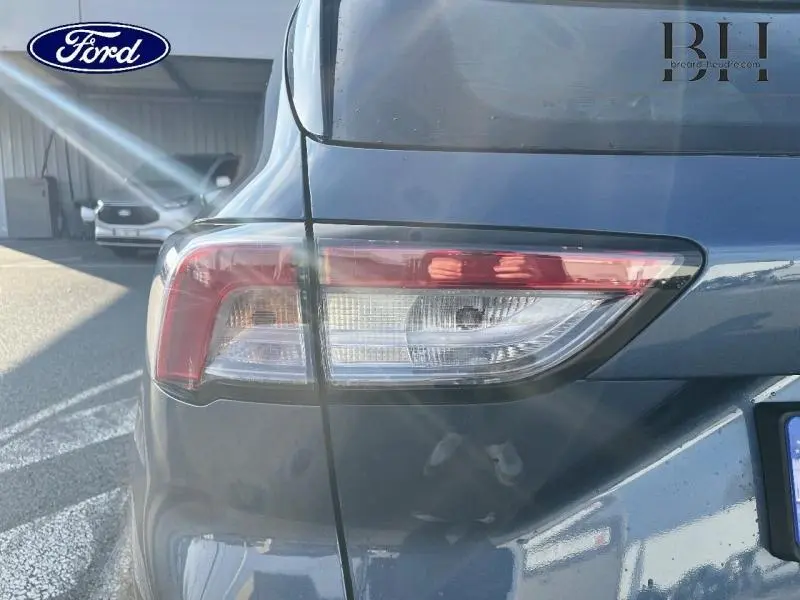 Gros plan sur le feu arrière droit d’un Ford Kuga 2023 bleu azur métallisé, avec reflets lumineux sur la carrosserie.