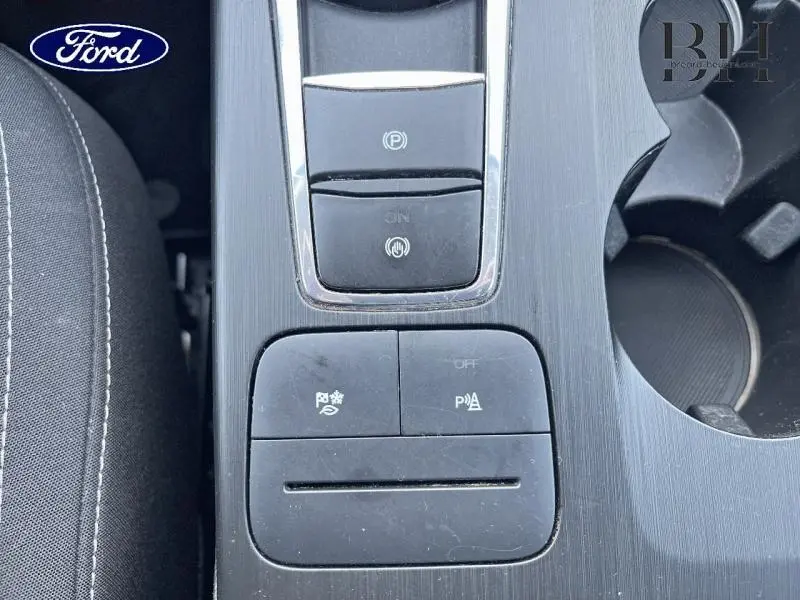 Vue plongeante sur la console centrale noire du Ford Kuga 2023, avec commandes électroniques et porte-gobelets.