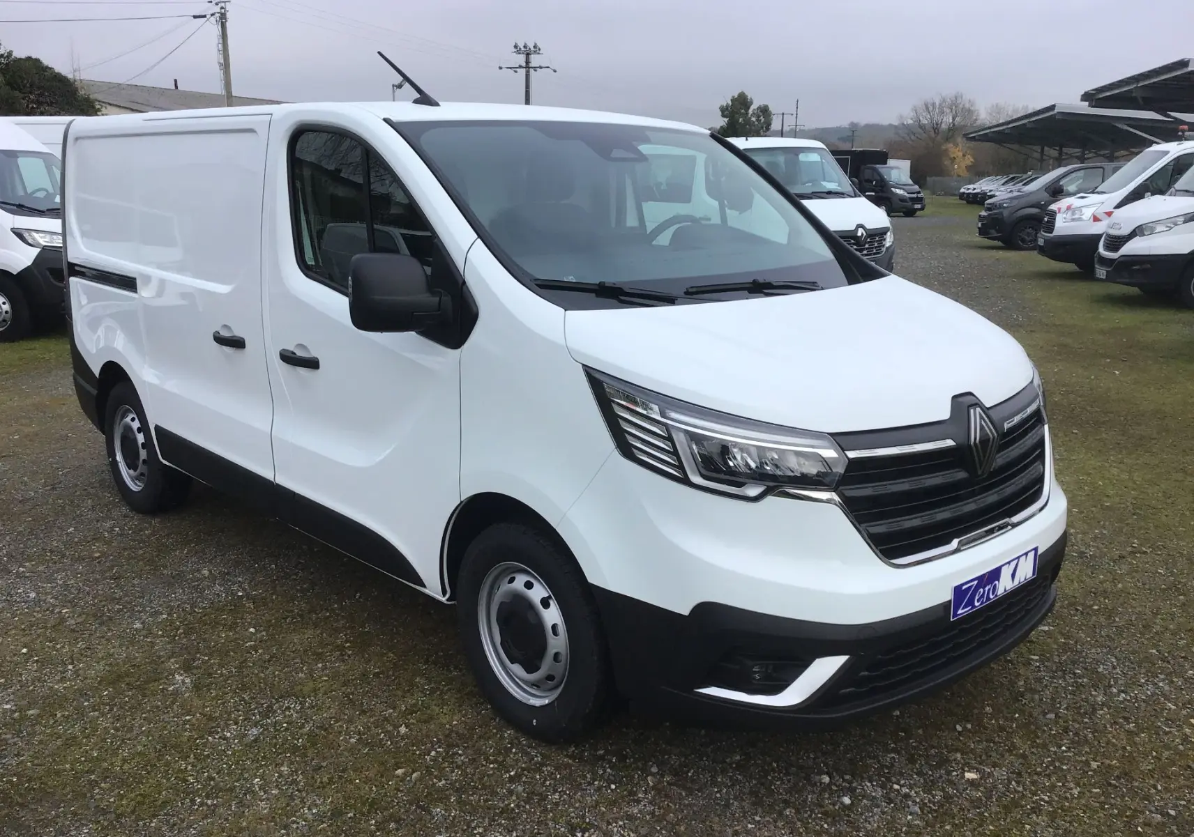Vue 3/4 avant droit d’un Renault Trafic Fourgon blanc 2025 avec calandre noire et feux LED distinctifs.