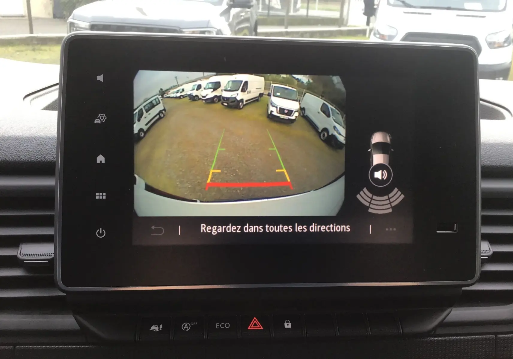 Écran tactile intérieur montrant la caméra de recul du Renault Trafic blanc, vue arrière avec plusieurs fourgons en stationnement.