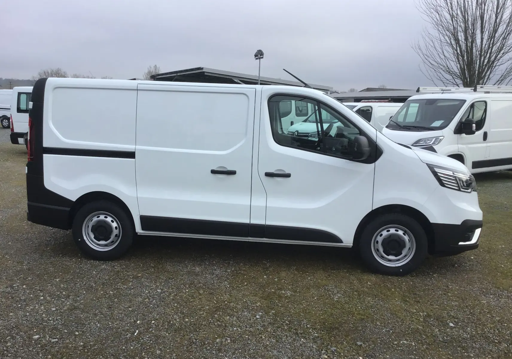 Vue de profil côté gauche d'un Renault Trafic Fourgon blanc avec portes latérales et jantes acier noires.