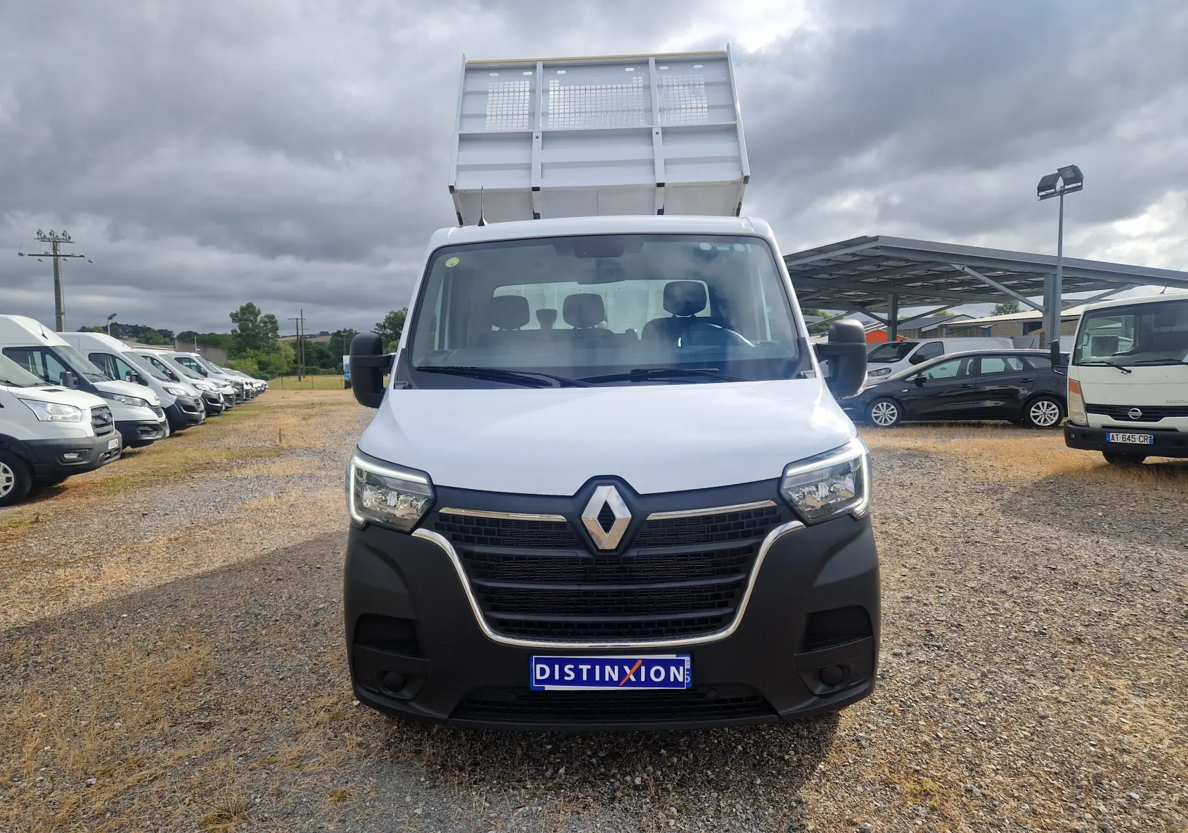 Vue avant d’un Renault Master Châssis Cabine blanc avec benne relevée sur un terrain extérieur sous ciel nuageux.