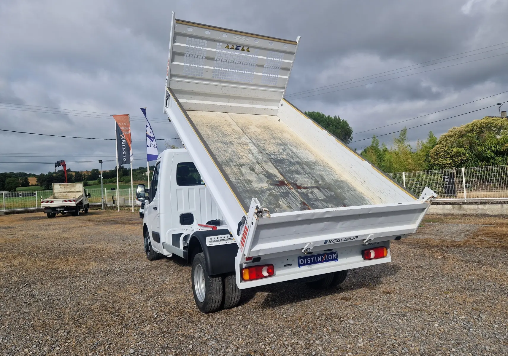 Renault Master Benne blanc vu de l'arrière droit, benne relevée et roues jumelées visibles sur sol gravillonné.