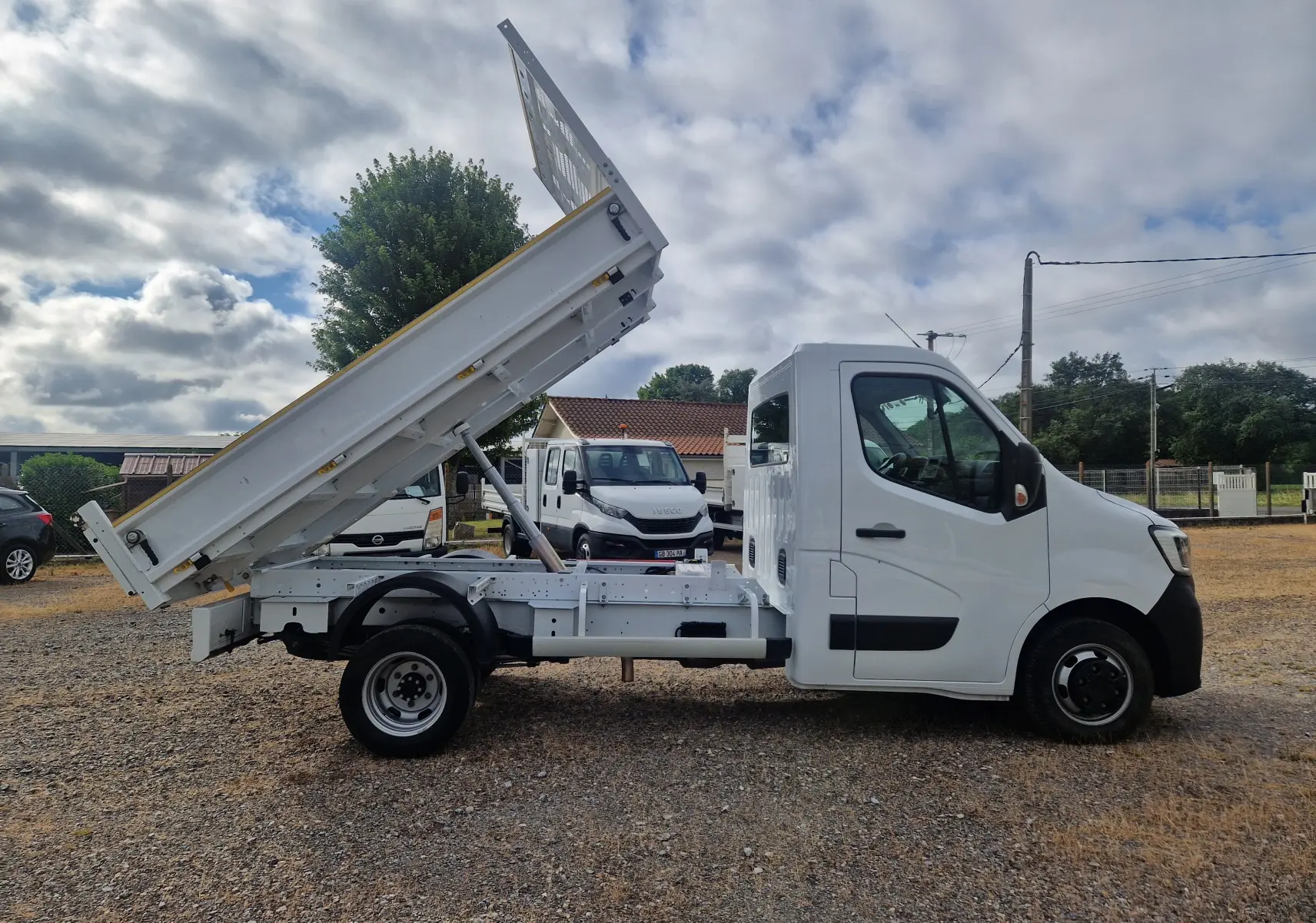 Vue latérale droite d’un Renault Master blanc avec benne relevée et roues jumelées sur terrain extérieur.