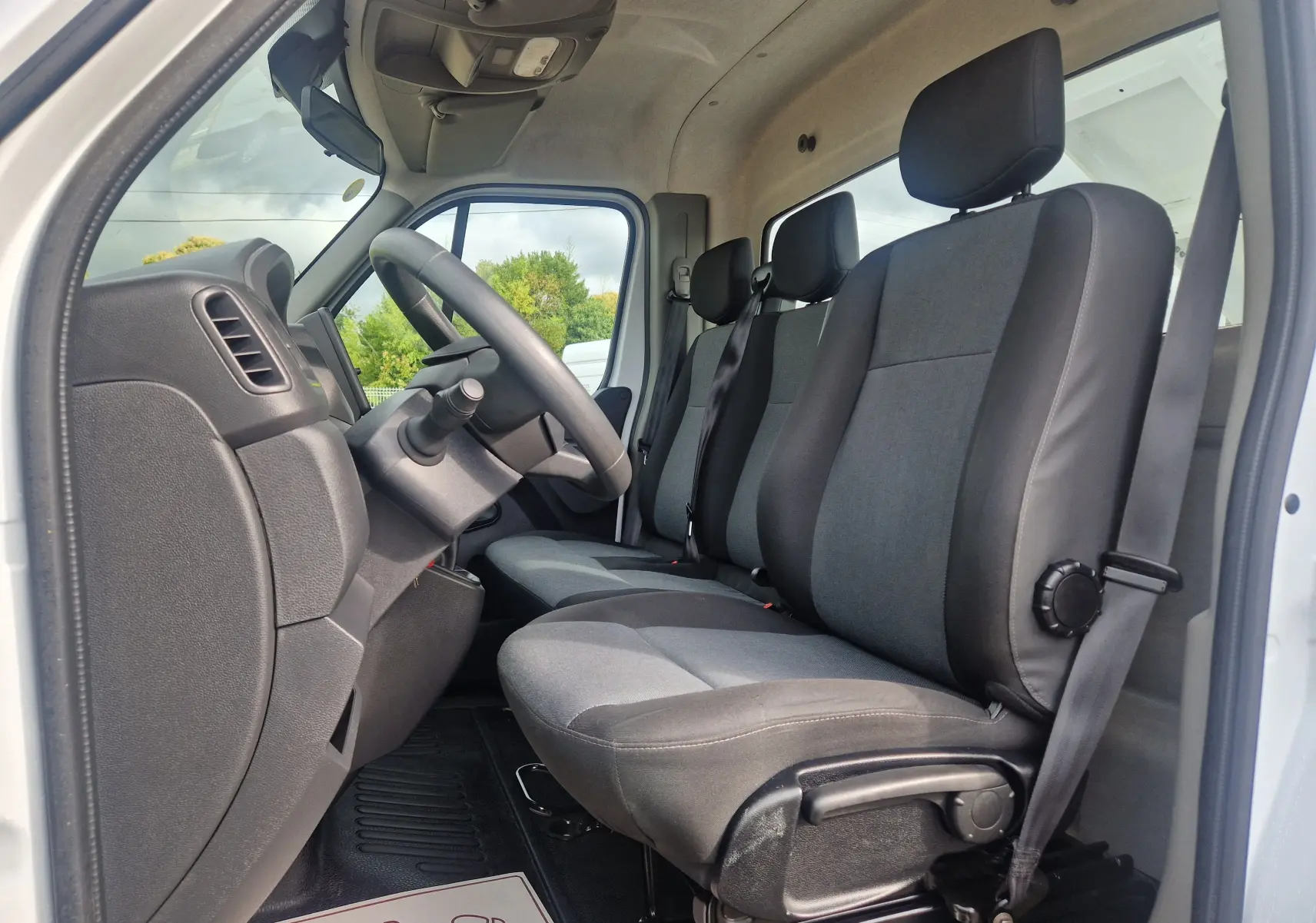 Vue intérieure côté conducteur du Renault Master Châssis Cabine blanc 2024, montrant les sièges tissu gris et noir et le volant.