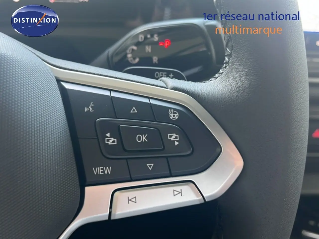 Gros plan sur les commandes gauche du volant noir du Volkswagen Tiguan 2026, avec boutons multifonctions et affichage digital en arrière-plan.