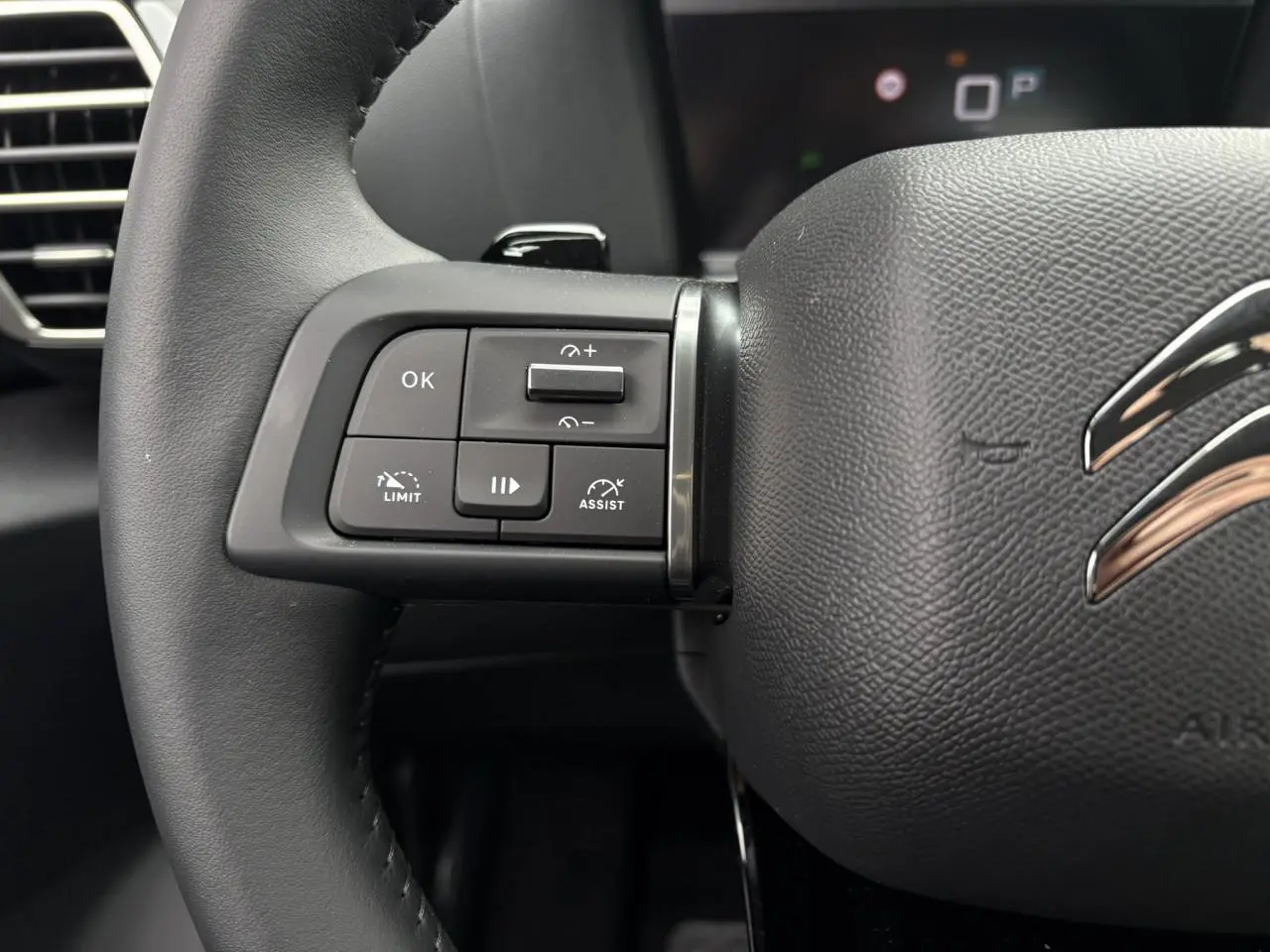 Gros plan sur la partie gauche du volant noir de la Citroën C4 2024 avec commandes intégrées et logo chromé.