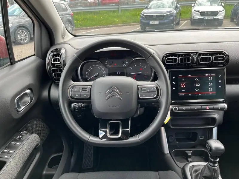 Vue frontale de l'habitacle du Citroën C3 Aircross gris acier, volant cuir et écran tactile central visible.