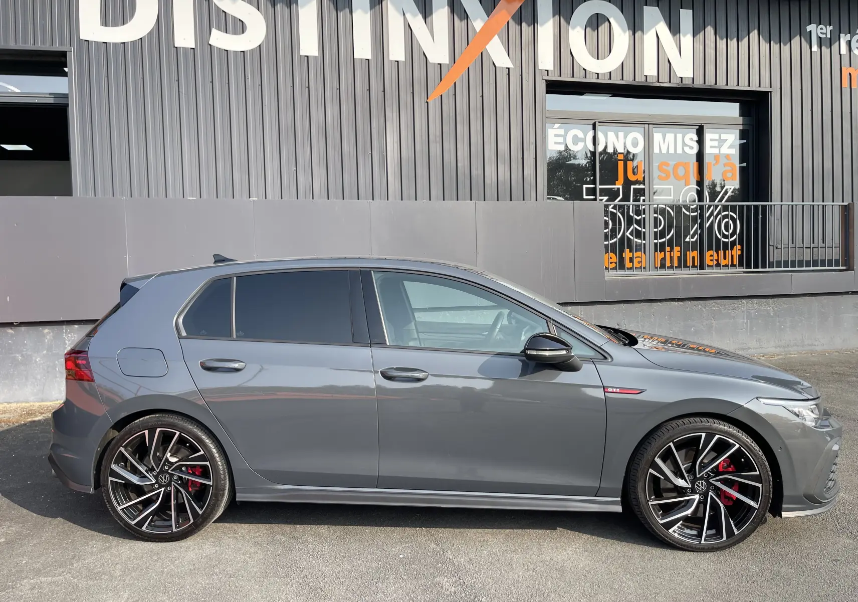 Profil côté gauche d'une Volkswagen Golf VIII GTI gris métallisé avec jantes noires à détails argentés et étriers rouges.