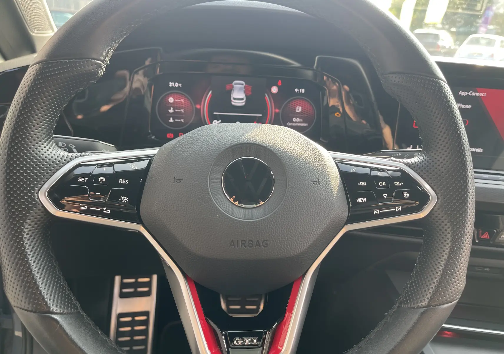 Vue rapprochée du volant cuir noir perforé de la Volkswagen Golf VIII GTI avec logo VW et badge GTI rouge.