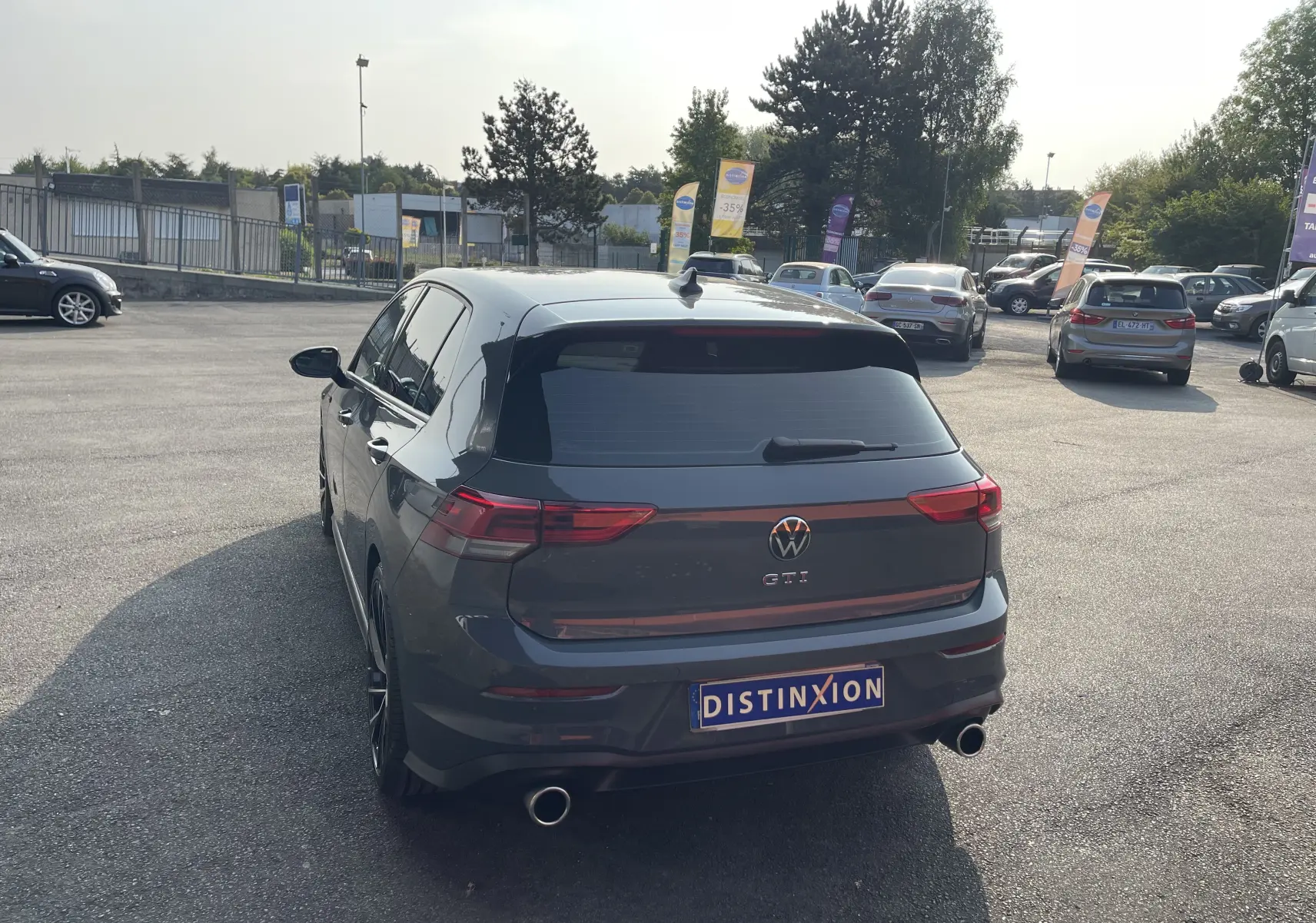 Vue 3/4 arrière d'une Volkswagen Golf VIII GTI gris métallisé avec double sortie d'échappement et vitres teintées.