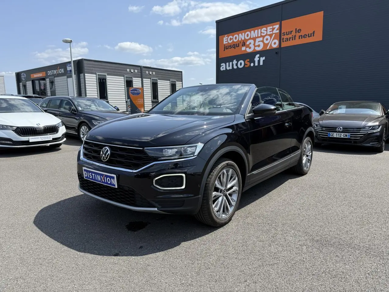 Volkswagen T-Roc Cabriolet noir nacré en 3/4 avant droit sur parking avec jantes alliage et capote ouverte.