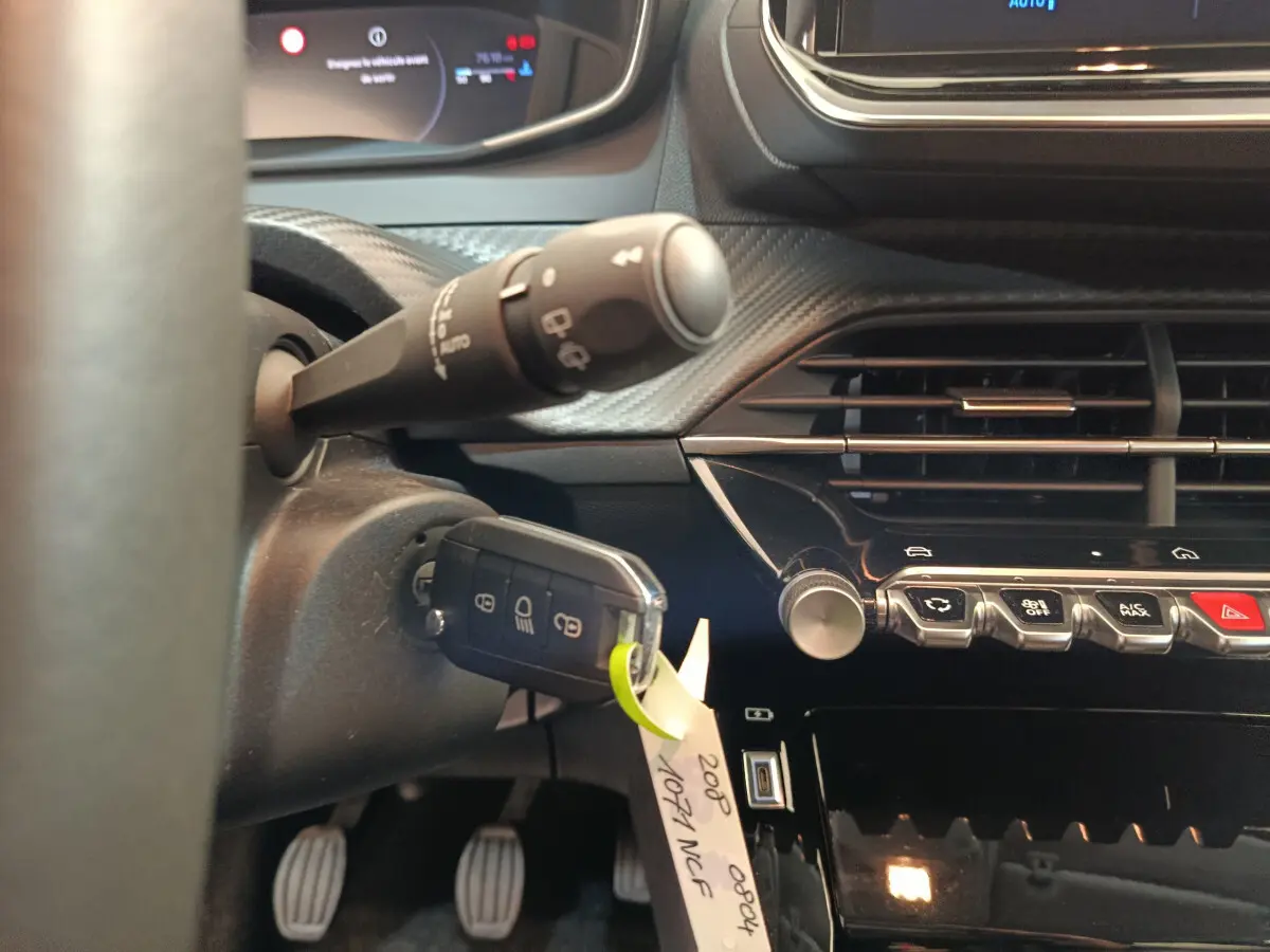 Gros plan intérieur sur le tableau de bord et clé de contact d'une Peugeot 208 gris clair, avec commandes et écran tactile visibles.
