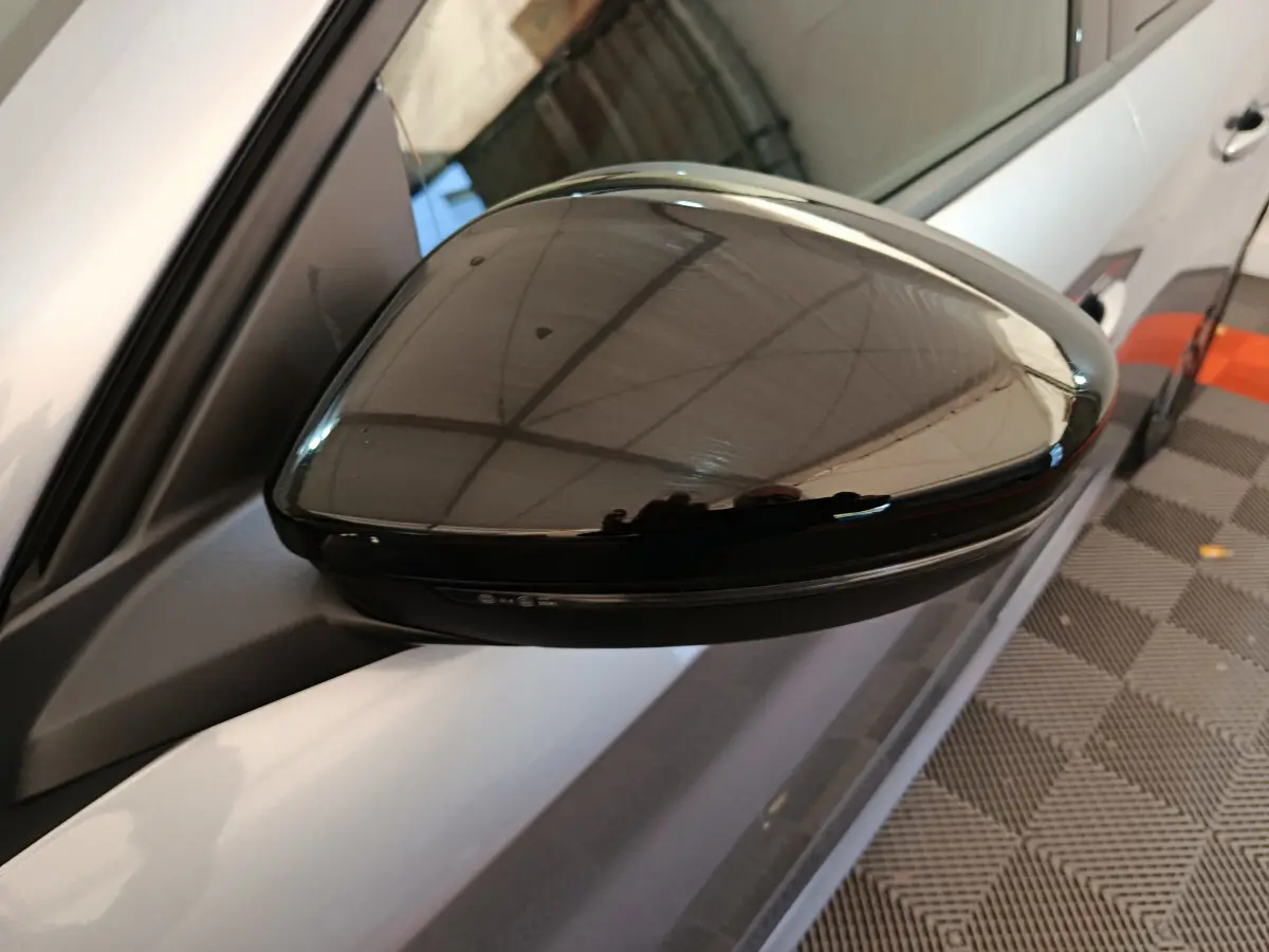 Gros plan sur le rétroviseur droit noir brillant d’une Peugeot 208 gris clair, avec clignotant intégré.