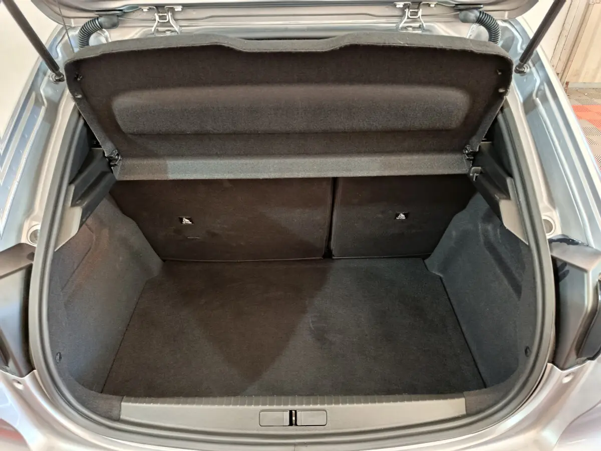 Coffre ouvert vu de l'arrière d'une Peugeot 208 gris clair, montrant l'espace de chargement vide et la tablette de séparation.