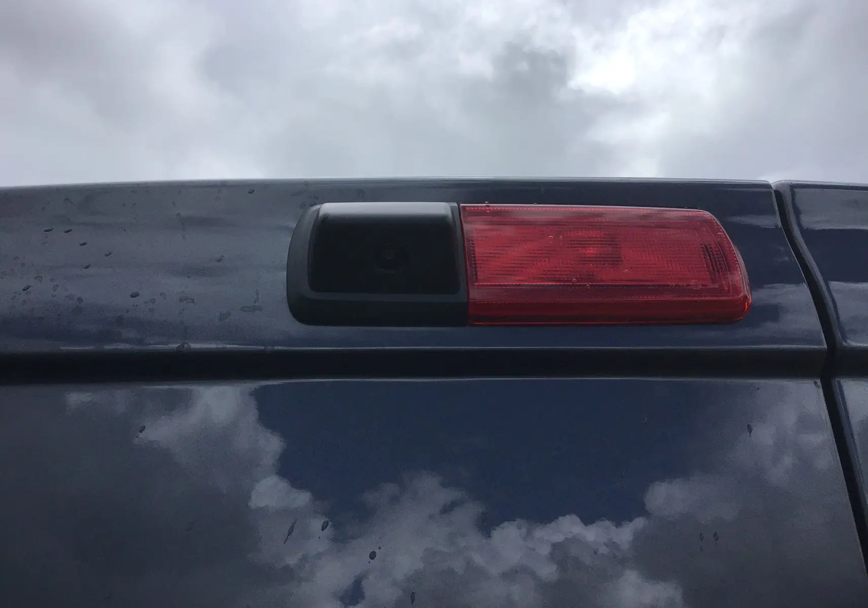 Gros plan sur la caméra de recul et le feu stop arrière du Renault Trafic Fourgon gris comète sous un ciel nuageux.