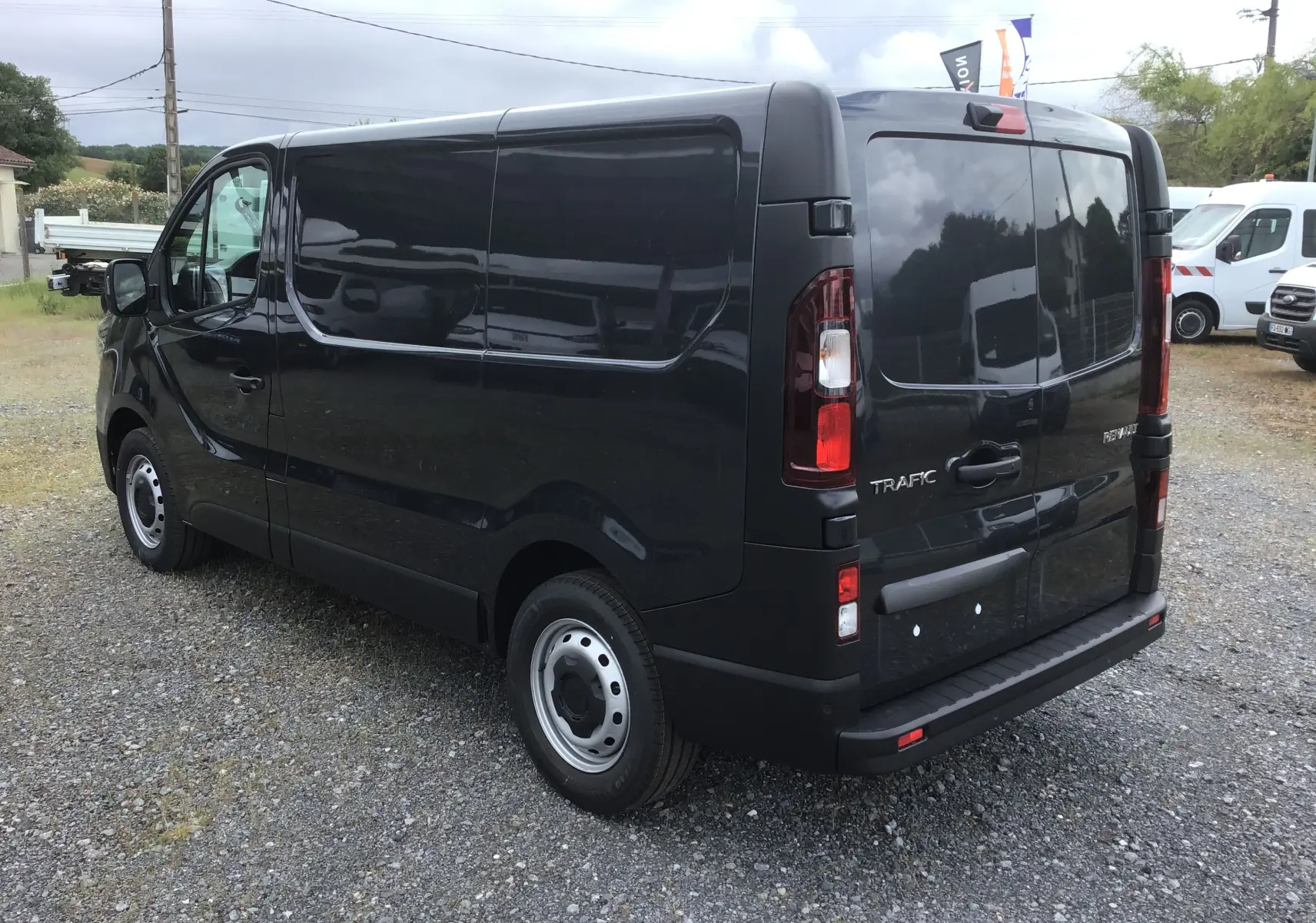 Vue 3/4 arrière droite d’un Renault Trafic Fourgon gris comète avec portes arrière fermées sur un sol gravillonné.