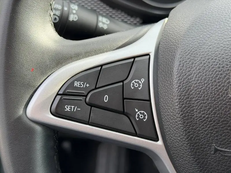 Gros plan sur les commandes de régulateur de vitesse à gauche du volant en cuir noir du Dacia Jogger Vert Cèdre métallisé 2025.