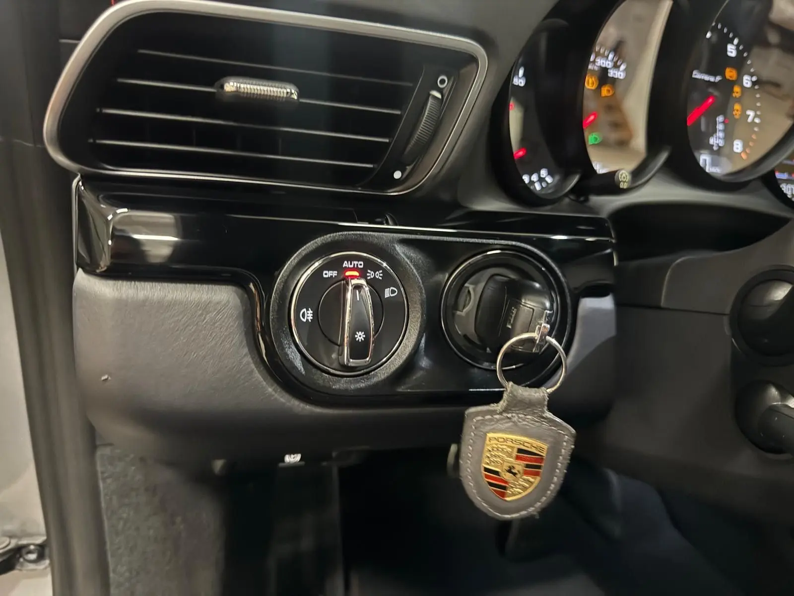 Gros plan sur le contacteur d’éclairage et la clé Porsche avec porte-clés dans l’habitacle noir d’une 911 991 Gris GT Silver.