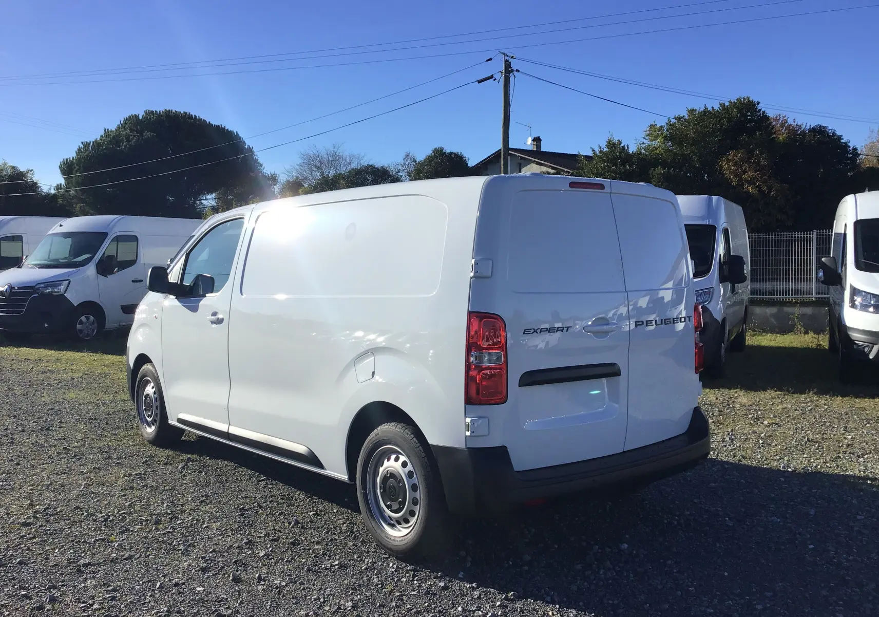Peugeot Expert Fourgon blanc vu en 3/4 arrière droit sur un parking ensoleillé avec plusieurs utilitaires.