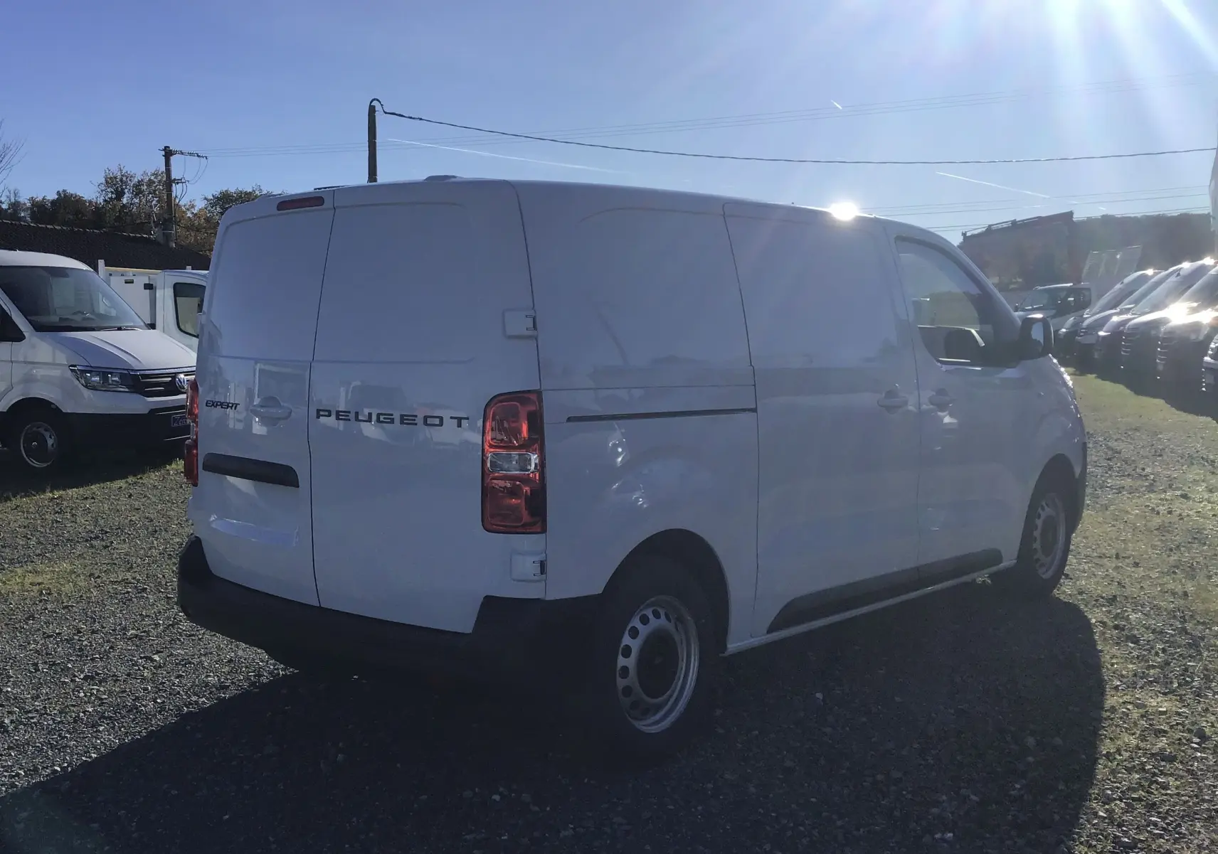 Peugeot Expert Fourgon blanc vu en 3/4 arrière droit sur un terrain avec plusieurs utilitaires stationnés.