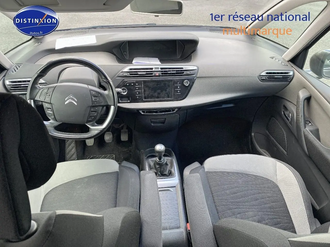 Intérieur avant de la Citroën C4 Picasso gris 2016, volant multifonction et boîte manuelle visibles, sièges tissu bicolore.