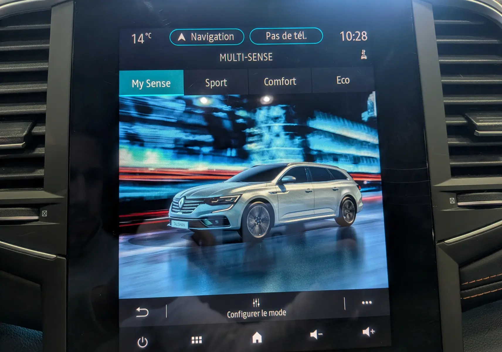 Écran tactile montrant une Renault Talisman Estate gris Cassiopé en 3/4 avant sur fond urbain flouté.