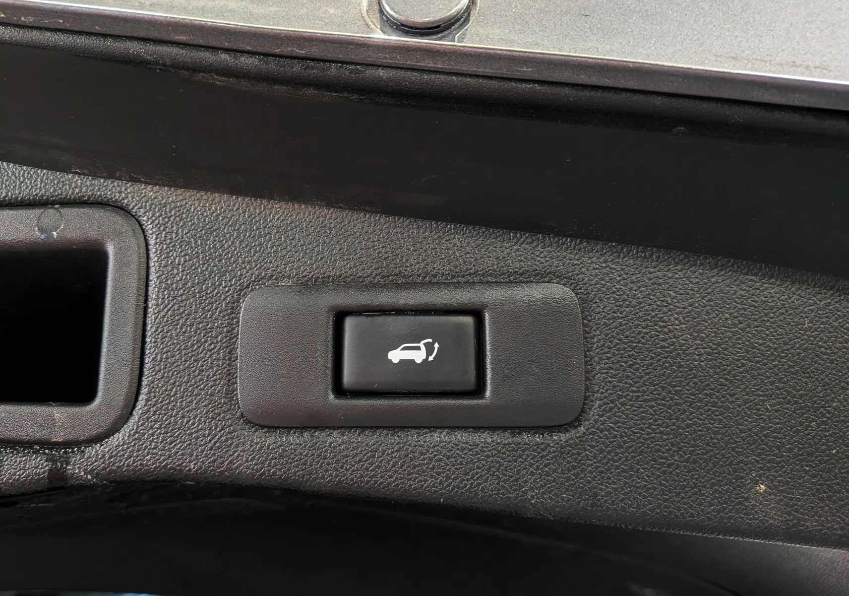 Bouton noir de commande d'ouverture électrique du hayon sur le coffre d'une Renault Talisman Estate gris Cassiopé.