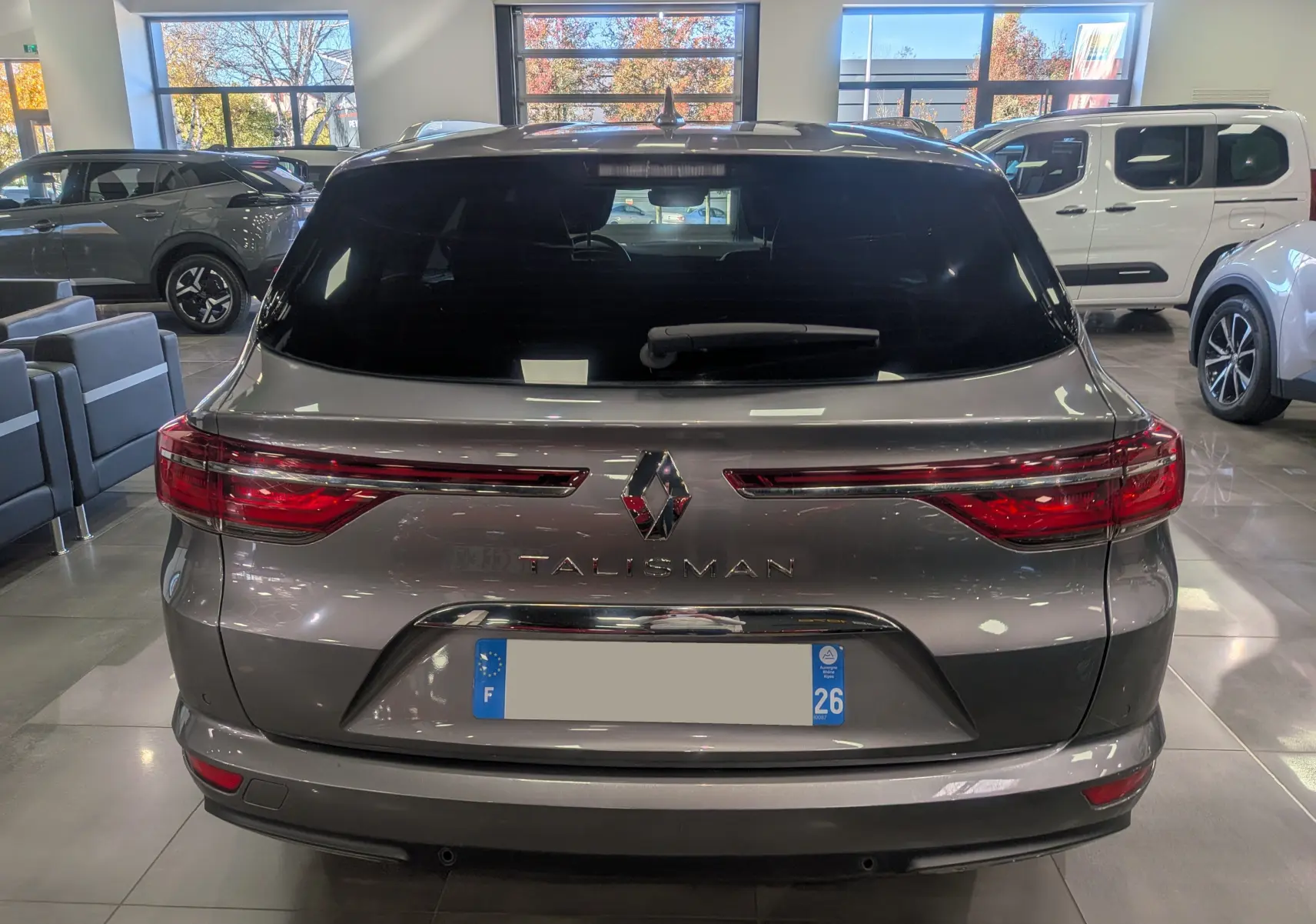 Vue arrière d'une Renault Talisman Estate gris Cassiopé dans un showroom, avec feux arrière allongés et logo central.