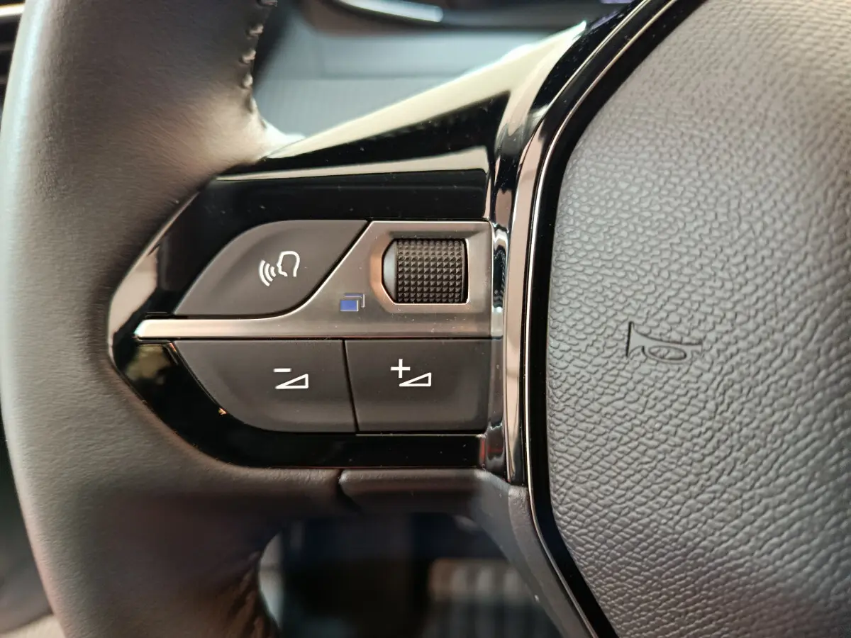 Gros plan sur les commandes vocales et volume au volant cuir noir d'une Peugeot 208 PureTech 100 S&S Allure 2025.