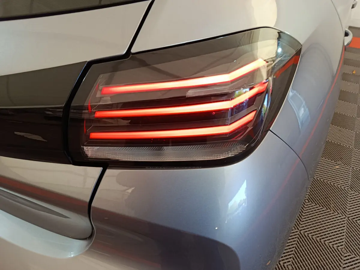 Gros plan sur le feu arrière droit allumé d’une Peugeot 208 gris clair, soulignant les lignes LED distinctives.
