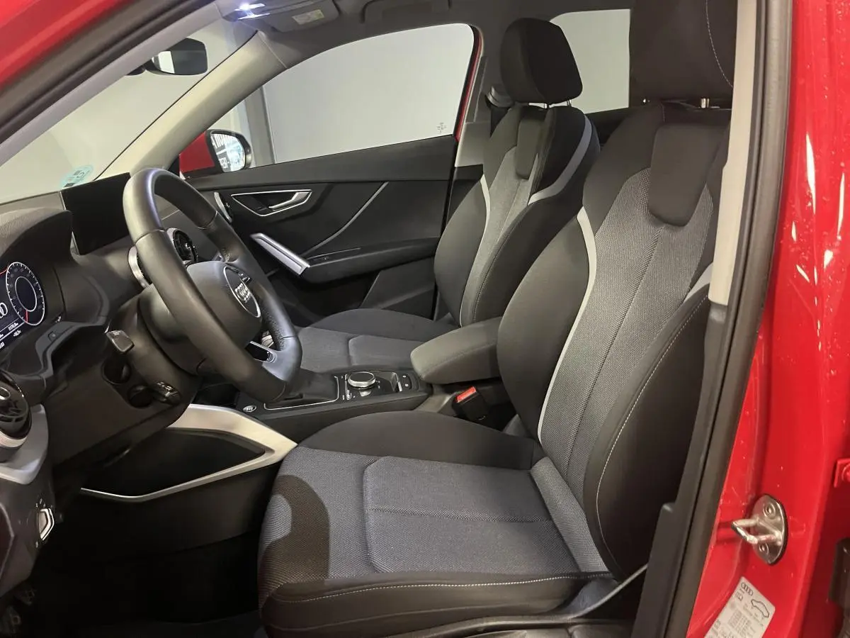 Vue intérieure côté conducteur de l'Audi Q2 rouge 2024, sièges sport noirs avec surpiqûres grises et volant cuir multifonction.