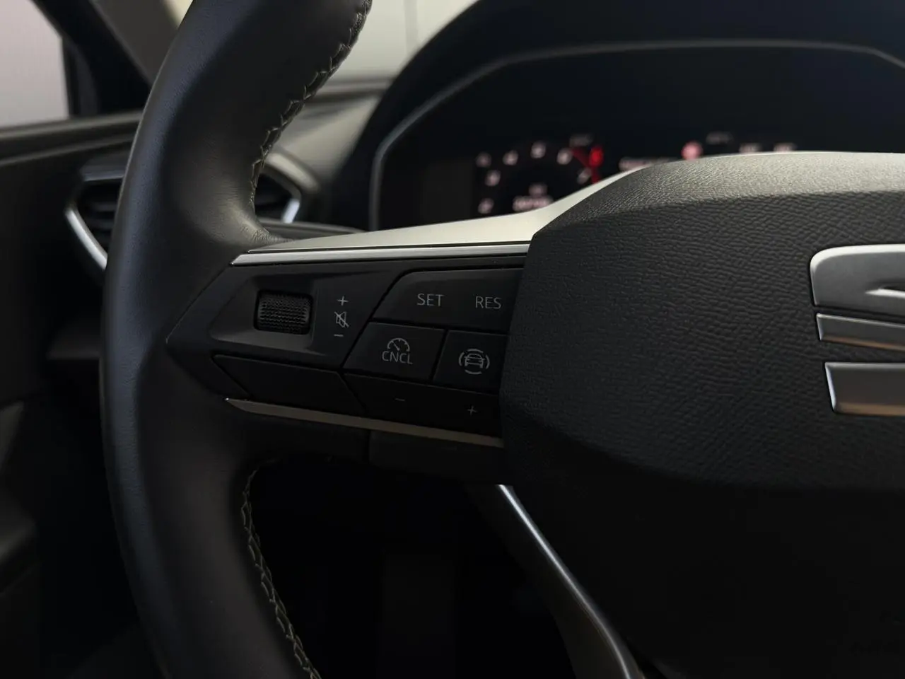 Gros plan sur le volant cuir multifonction de la SEAT LEON ST 1.5 TSI, avec commandes de régulateur et logo SEAT visible.
