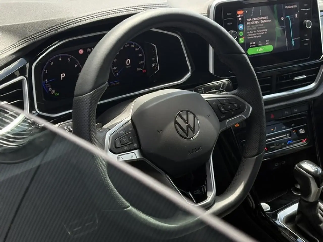Vue rapprochée du volant multifonction noir et du tableau de bord digital du Volkswagen T-Roc 2025, avec écran tactile et levier de vitesse.