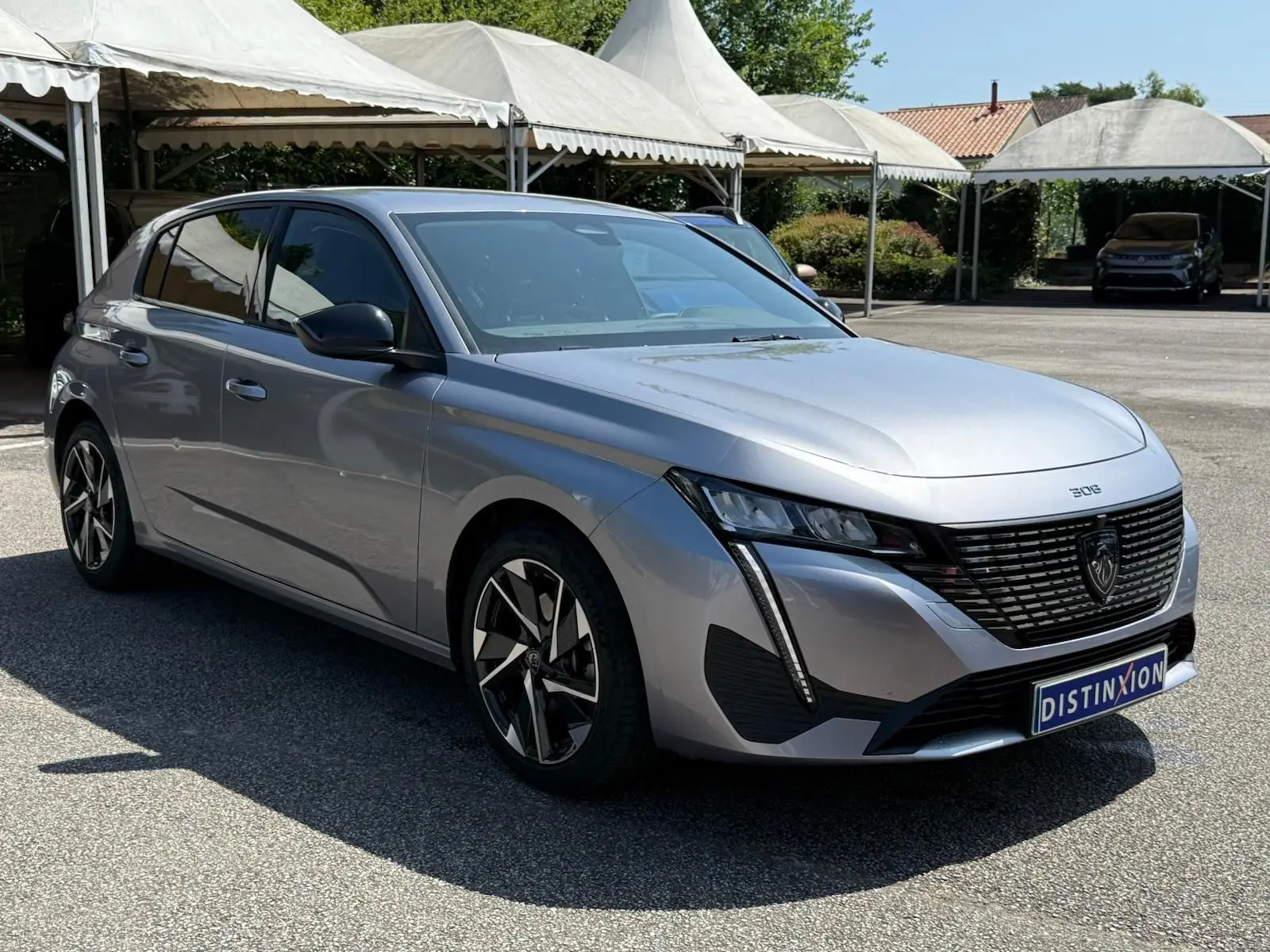 Peugeot 308 gris Artense vue 3/4 avant droit, avec calandre noire et feux LED verticaux distinctifs.