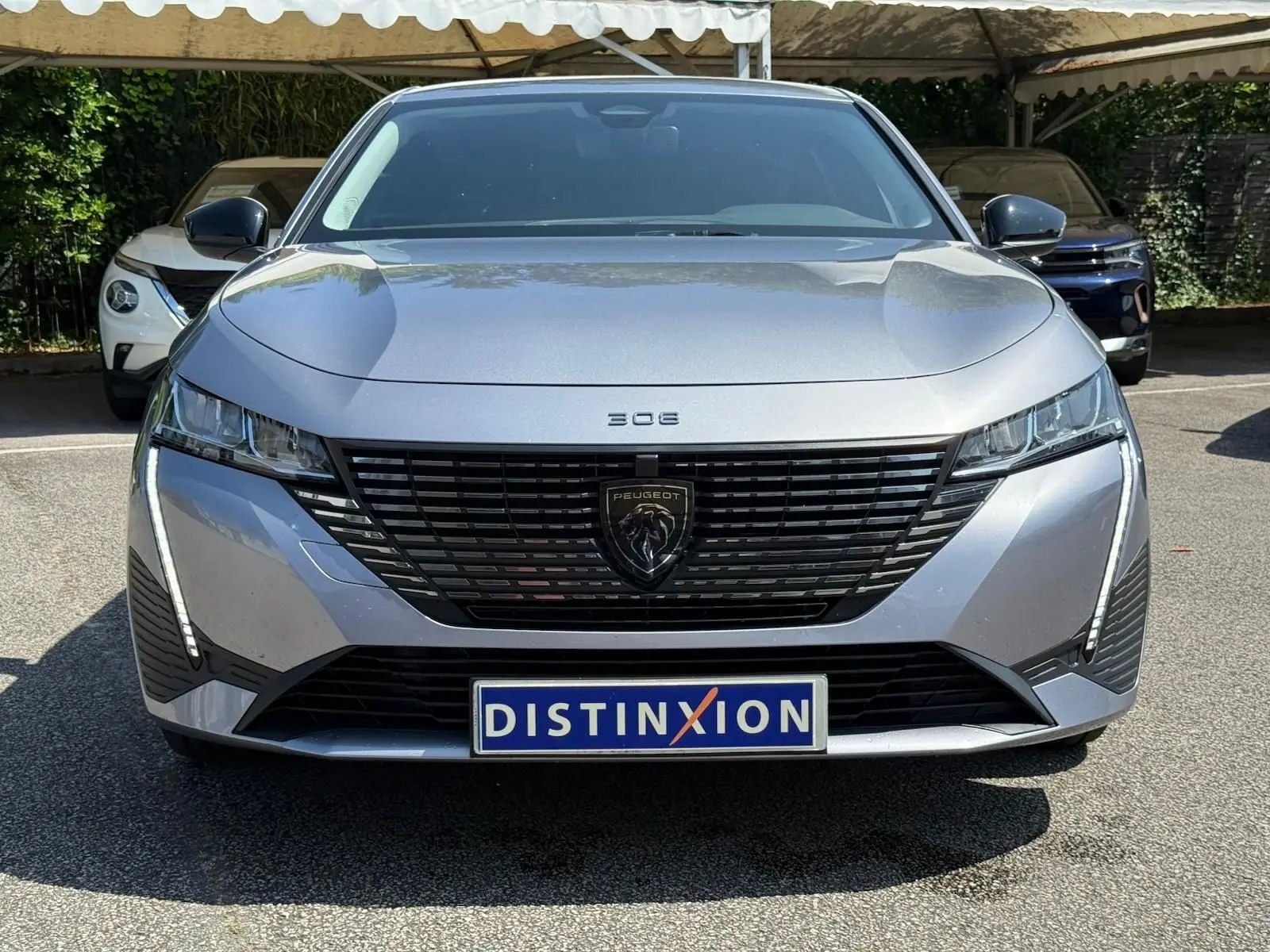 Vue frontale d'une Peugeot 308 2024 gris Artense avec calandre noire et feux LED en forme de griffes.
