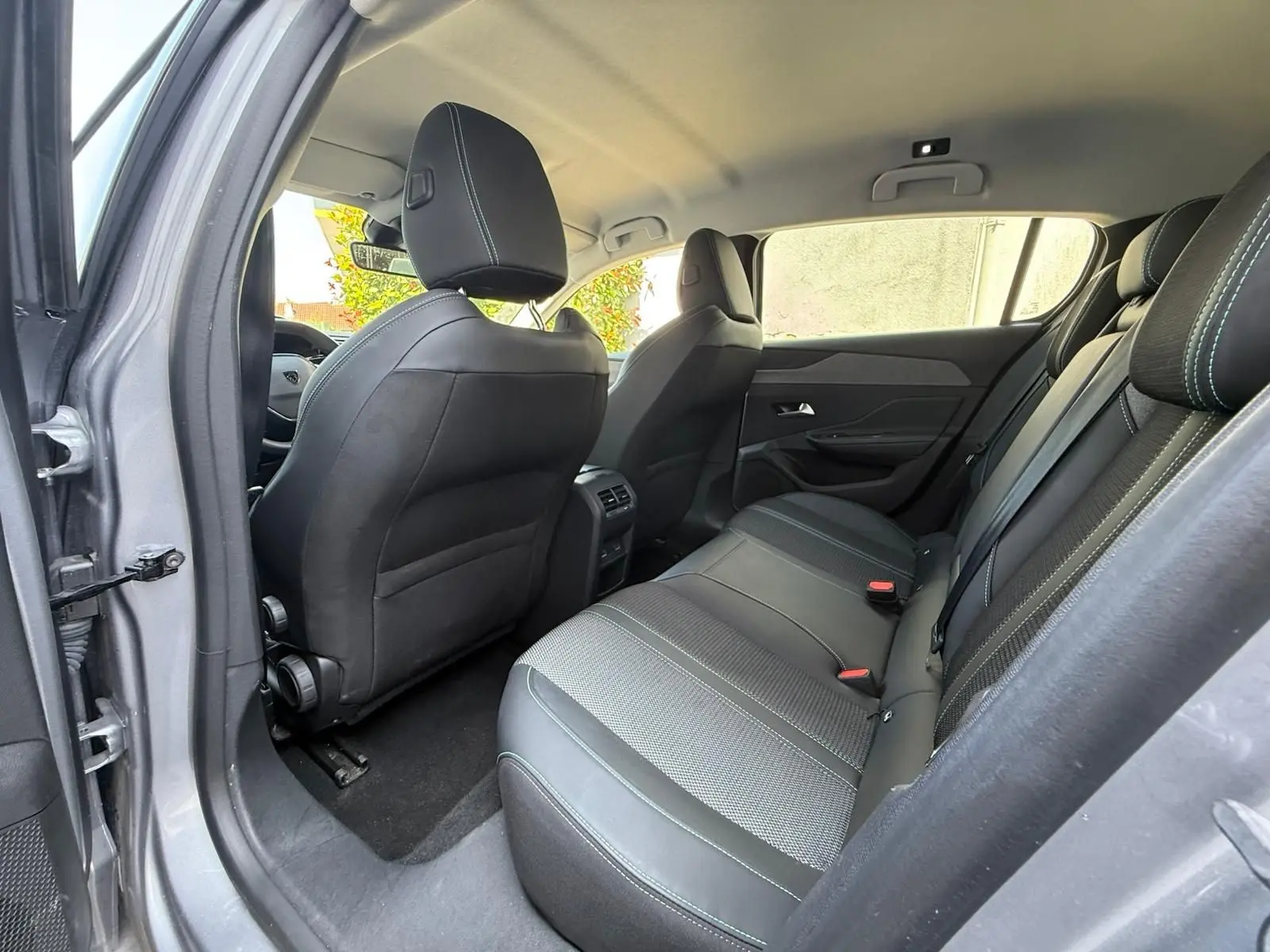 Vue intérieure arrière côté gauche de la Peugeot 308 2024 gris Artense, montrant les sièges arrière en tissu et cuir noir.